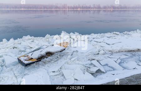 Zerstörtes Boot auf einem gefrorenen Donau-Fluss mit fantastischem Sonnenuntergang in der Nähe von Belgrad, Zemun, Serbien Stockfoto