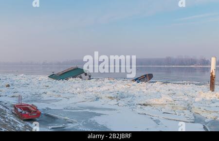 Holzhaus und zwei an der gefrorenen Donau eingeschlossene Boote, in der Nähe der Stadt Belgrad, viele Eisteile, mit fantastischer Fluss- und Himmelslandschaft Stockfoto