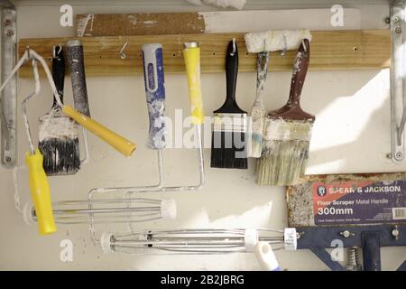 Malerwerkzeuge, eine Auswahl gebrauchter Farbbürsten und Farbrollerrahmen, Schaber, die Haken in einem Schrank eines Handwerkers zum Malen und Dekorieren hängen Stockfoto