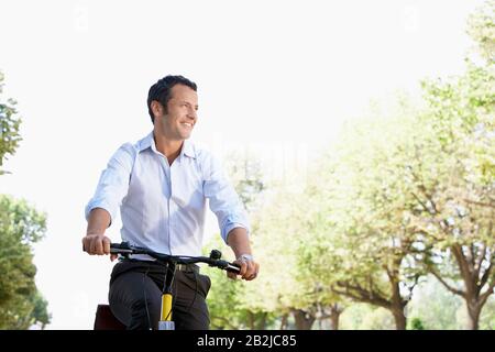 Unternehmer fahren Fahrrad im Park im niedrigen Winkel Stockfoto