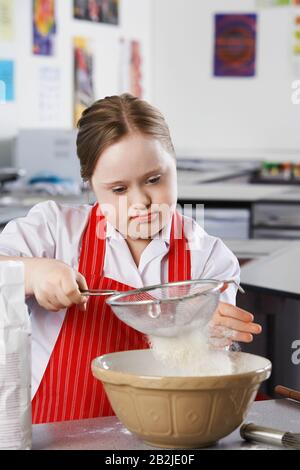 Mädchen (10-12) mit Down-Syndrom Mehl in Schüssel sieben Stockfoto