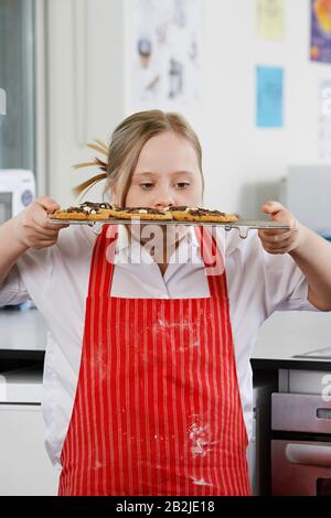 Mädchen (10-12) mit Down-Syndrom, das Plätzchen auf dem Backblech in der Küche trägt Stockfoto