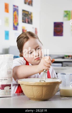 Mädchen (10-12) mit Down-Syndrom mit Schneebesen, um Inhalt in der Schüssel zu rühren Stockfoto