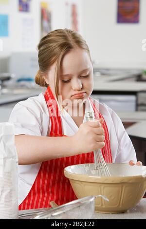 Mädchen (10-12) mit Down-Syndrom mit Schneebesen, um Inhalt in der Schüssel zu rühren Stockfoto
