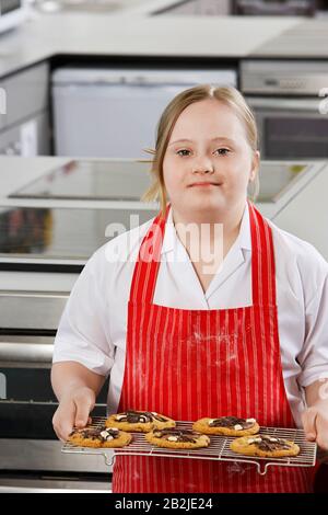 Portrait des Mädchens (10-12) mit Down-Syndrom, das Plätzchen auf dem Backblech trägt Stockfoto