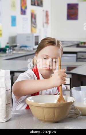 Mädchen (10-12) mit Down-Syndrom, das Inhalte in der Schüssel mischt Stockfoto