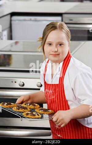 Portrait des Mädchens (10-12) mit Down-Syndrom, das Plätzchen auf dem Backblech trägt Stockfoto