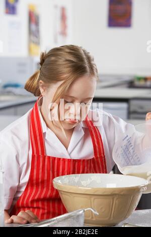 Mädchen (10-12) mit Down-Syndrom, das Milch in die Schüssel gießt Stockfoto