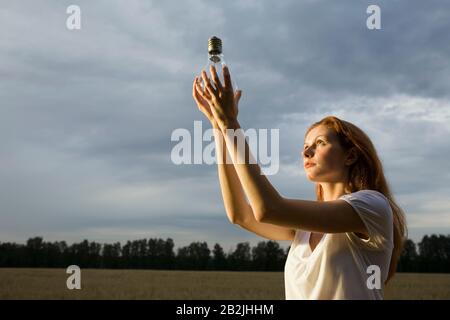 Junge Frau in einem Feld, die eine Glühbirne hält Stockfoto
