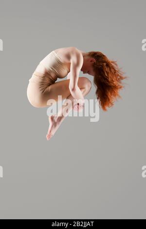 Tänzerin in Mittelluft mit Armen um die Knie Stockfoto