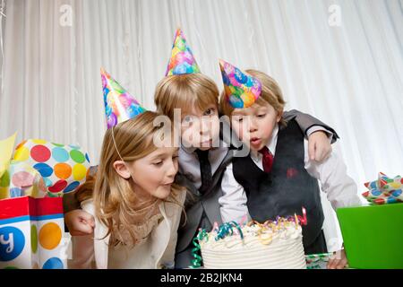 Brüder und Schwester blästen zusammen Kerzen auf Geburtstagskuchen Stockfoto