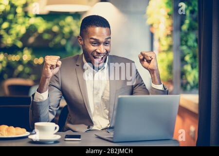 Aufgeregter schwarzer Mann feiert seinen Sieg im Café Stockfoto