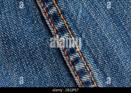 Detaillierte Nahaufnahme des blauen Denim-Materials mit strukturiertem Gewebe und diagonalem Twill-Muster. Eine Naht verläuft diagonal über das Bild, hervorgehoben durch hellorangefarbene Nähte, die einen Kontrast bilden Stockfoto