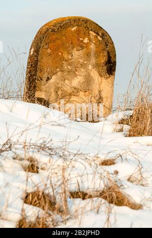 Ein großes, abgerundetes, verwittertes Steindenkmal steht aufrecht auf einem schneebedeckten Feld. Die Steinoberfläche ist mit Flecken aus orangefarbenen und braunen Flechten, Rissen und Erosion strukturiert, was das Alter und angibt Stockfoto