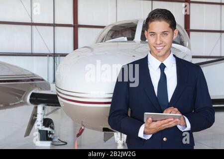 Portrait von gut aussehenden jungen Piloten mit Tablet-PC vor dem Flugzeug Stockfoto