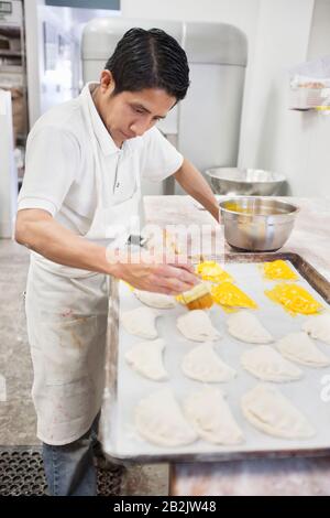 Junger männlicher Bäcker, der sich mit der Zubereitung von Gebäck in der Backküche beschäftigt Stockfoto
