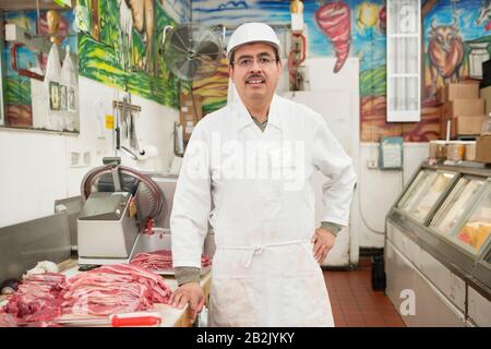 Porträt eines Metzgers, der Schürze in der Nähe von Fleisch im Laden trägt Stockfoto