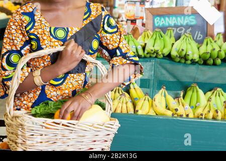 Mittelteil von afroamerikanischem in traditioneller Kleidung mit Gemüsekorb auf dem Supermarkt Stockfoto