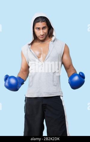 Porträt eines selbstbewussten jungen Mannes, der Boxhandschuhe trägt, die über blauem Hintergrund stehen Stockfoto
