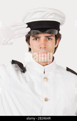 Porträt des jungen Marine-Beamten, der vor grauem Hintergrund salutiert Stockfoto