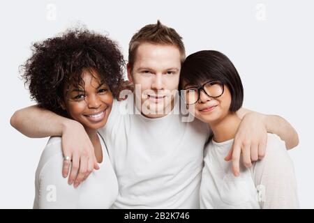 Porträt des jungen kaukasischen Mannes mit seinen Armen um zwei weibliche Freunde über weißem Hintergrund Stockfoto