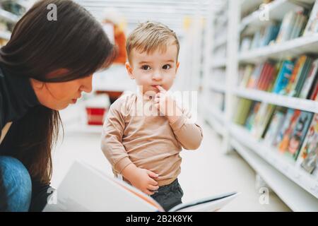 Süßes Kleinkind im Buchladen mit Mutter mit offenem Buch Stockfoto