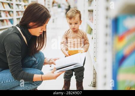 Süßes Kleinkind im Buchladen mit Mutter mit offenem Buch Stockfoto