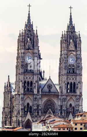 Eine hohe Kathedrale im gotischen Stil mit zwei symmetrischen Türmen mit spitzen Türmen, von denen jeder mit einem Kreuz gekrönt ist. Die Türme zeigen große Zifferblätter mit blauen Zeigern und Ziffern. Die Fassade umfasst Stockfoto