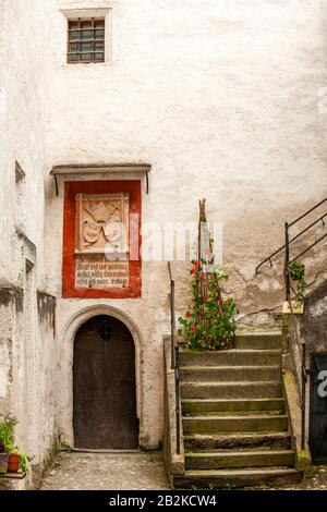 Ein schmaler Innenhof verfügt über eine verwitterte Steintreppe mit Metallgeländern, die nach oben führen und von einer weiß getünchten Steinmauer flankiert werden. Unterhalb der Treppe befindet sich eine dunkle Holzbogentür mit einer kleinen Stockfoto
