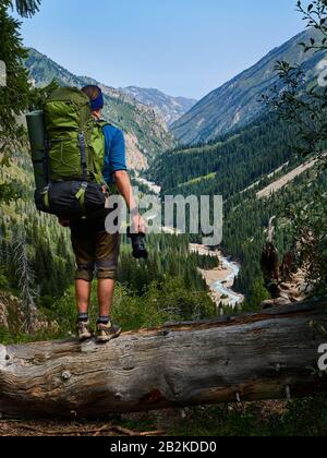 Guy Fotograf mit einem Rucksack auf dem Rücken und einer Reflexkamera in den Händen. Mann in blauem Hemd steht am Rande eines Bergweges. Guy ist ein Mitarbeiter Stockfoto