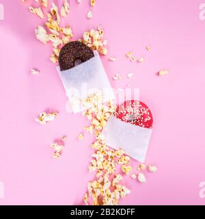 Doughnuts und Popcorn auf einem rosafarbenen Hintergrund. Flaches Lay. Stockfoto