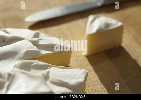 Camembert-Käse mit einer Dreiecksscheibe und einem Messer auf einem Holzbrett. Stockfoto