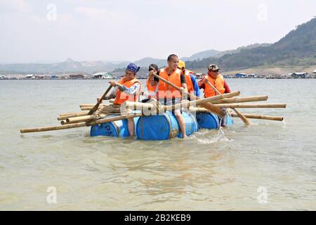 Eine Gruppe von Jugendlichen rudert in einem Survival-Training im Freien ein Notboot aus Bambusstäbchen, Plastikfässern und Seilen. Stockfoto