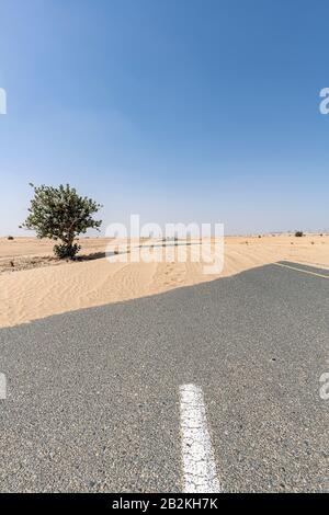 Vertikaler Schuss von einer leeren Straße, die in der Wüste von Sand bedeckt ist, mit blauem Himmel und ohne Wolken Stockfoto