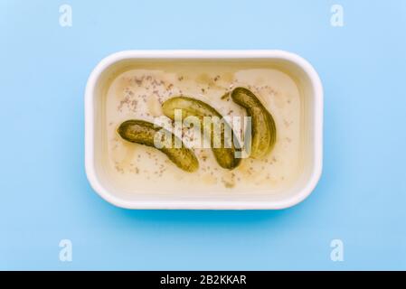 Eingepickte Gurken in einem metallisch weißen Behälter. Drei Pickel in einem Mixbecher auf blauem Hintergrund Stockfoto