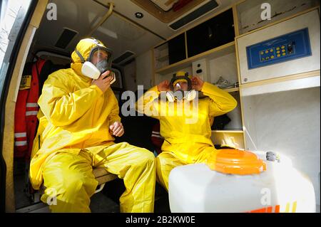 Sanitäter sitzen im Rettungswagen und tragen gelbe Schutzkleidung und Masken zur Desinfektion von Coronavirus, Training. Februar 202 Stockfoto