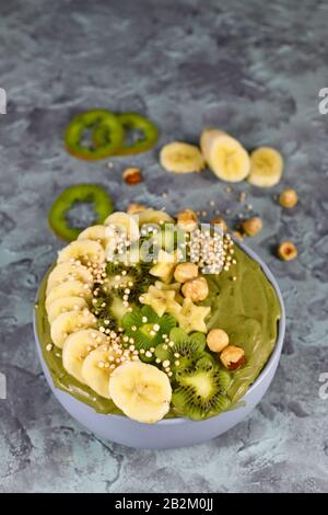 Smoothie-Schüssel aus grünem Obst mit sternförmigen Bananen, Kiwi, Haselnuss und gebucktem Quinoa-Korn auf grauem Grund Stockfoto