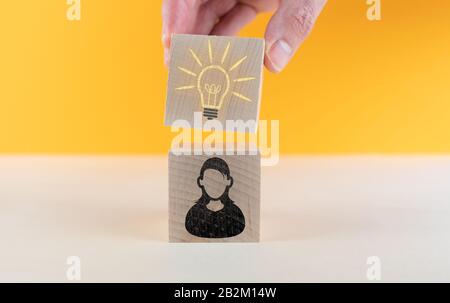 Person mit Ideenkonzept, weiblichem Avatar-Symbol und glühender Glühlampe auf Holzwürfeln vor orangefarbenem Hintergrund Stockfoto