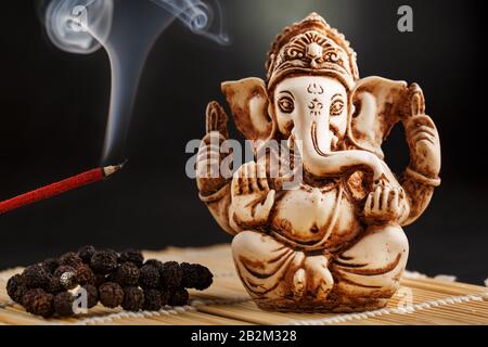 Ganesha auf schwarzem Hintergrund. Statue und Rosary mit rotem Räucherstäbchen Ganesha Sahasranama Stockfoto