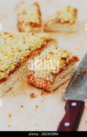 Süßer Sandtart mit Aprikosenmarmelade. In Stücke schneiden, auf einem Brett liegend mit einem Wasserkocher im Hintergrund. Teekanne mit Teetassen und süßem Kuchen Stockfoto