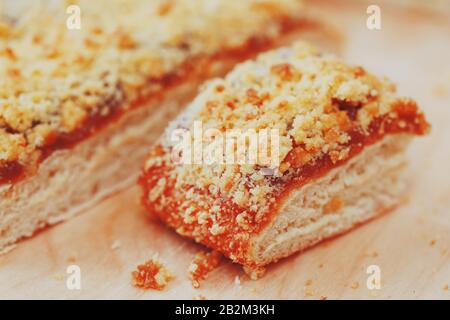 Süßer Sandtart mit Aprikosenmarmelade. In Stücke schneiden, auf einem Brett liegend mit einem Wasserkocher im Hintergrund. Teekanne mit Teetassen und süßem Kuchen Stockfoto