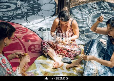 Maroochydore, Australien - 15. Februar 2020. Weibchen weben Körbe auf Handwerkerwerkstatt, sitzen auf Teppich im Park. Vielfalt und Einbeziehung in Kreativität. Frauengemeinschaft. Australien multikulturell. Stockfoto