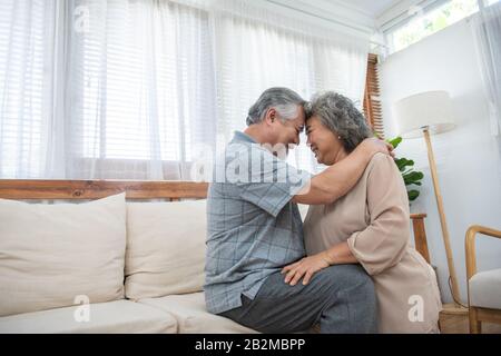 Lachende Rentner hübsches asiatisches Paar, das zu Hause auf der Couch sitzt, Ehepartner, die ein gesundes, zauberndes Lächeln und Zahnpflege für alte gehabt haben Stockfoto