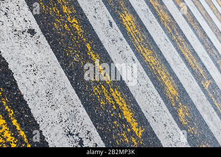 Fußgängerüberweg, gelbe und weiße Streifen auf nassem Asphalt in Form von Textur und Untergrund. Abgenutzte und abgenutzte Streifen eines Fußgängerübergangs. Stockfoto