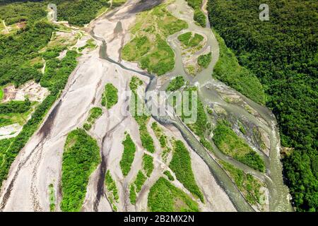 Ein Luftbild zeigt einen sich windenden Fluss, der durch eine Landschaft mit erheblicher Entwaldung schneidet. Der Fluss fließt durch eine Mischung aus freiliegender, heller Erde und Flecken von dichtem Grün Stockfoto