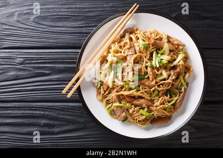 Leckere, gebratene chinesische Eiernudeln mit napa Kohl-Grünzwiebeln und Schweinefleisch in einem Teller auf dem Tisch, Horizontale Draufsicht von oben Stockfoto