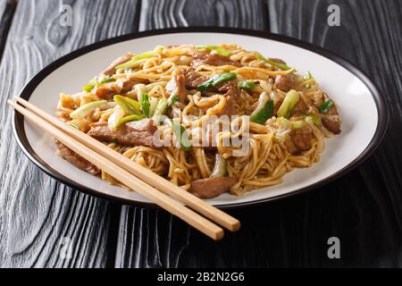 Pikante Shanghaier Eiernudeln mit Chinakohl, grünen Zwiebeln und Schweinefleisch in einem Teller auf dem Tisch. Horizontal Stockfoto