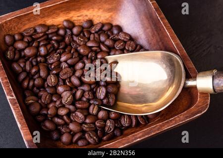 Kaffeethema. Platte mit Kaffeebohnen auf schwarzem Holztisch. Vintage-Kupferschaufel. Stockfoto