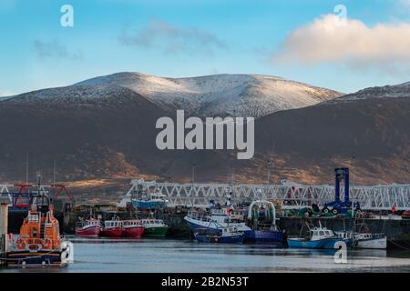 Fenit, Irland - 2. März 2020: Fischerboote, die im Hafen von Fenit an der Westküste des County Kerry angedockt waren, kaperte Snow die Halbinsel Dingle im Rücken Stockfoto