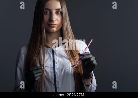 Das Studentenporträt eines Mädchens in einem weißen Mantel, ein Zahnarztarzt in Handschuhen, hält medizinische Instrumente. Auf grauem Hintergrund. Zahnärztin. Dramatischer medizinischer por Stockfoto